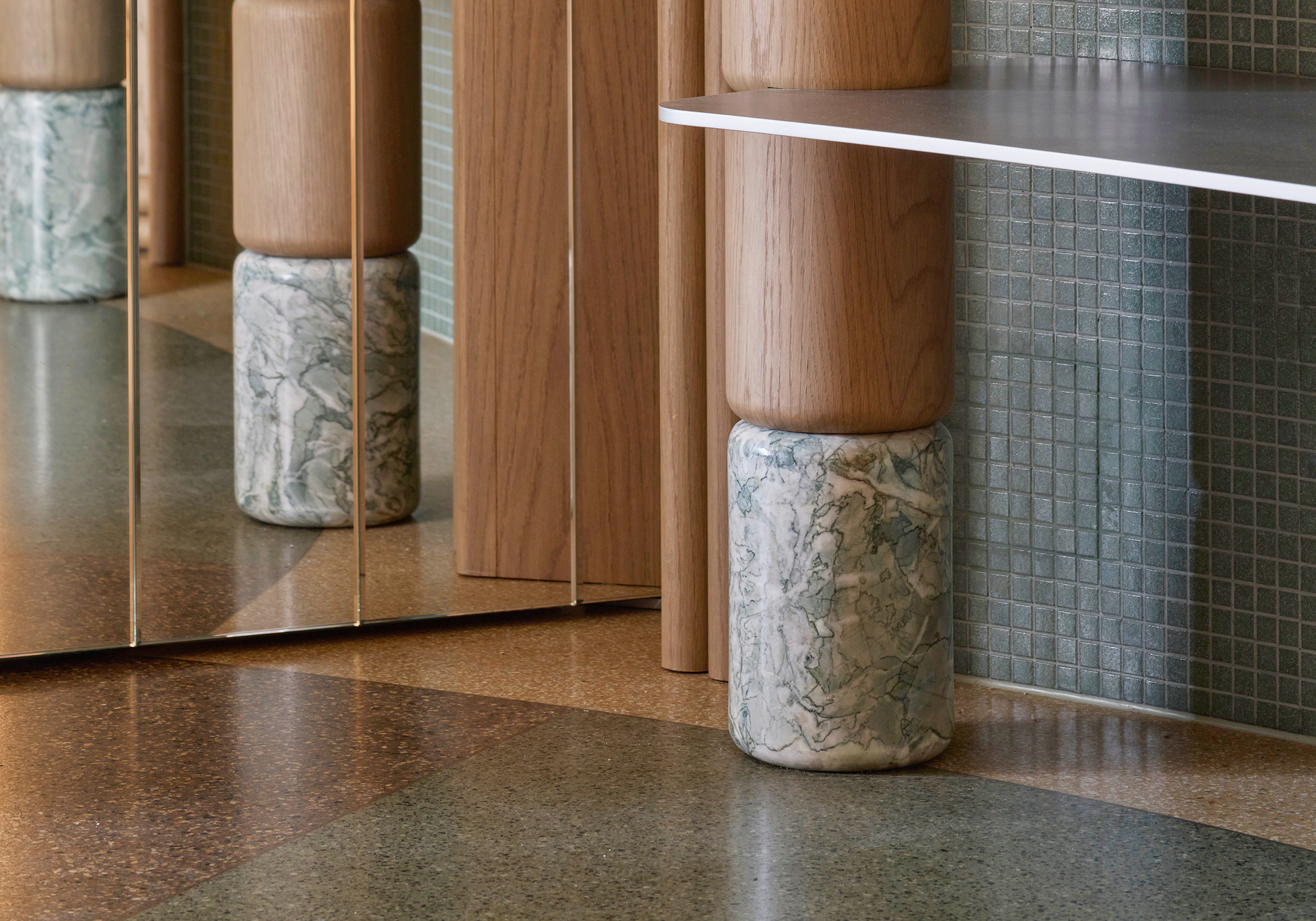 Detail of oak column on marble base beside mirrored panel and mosaic tile
