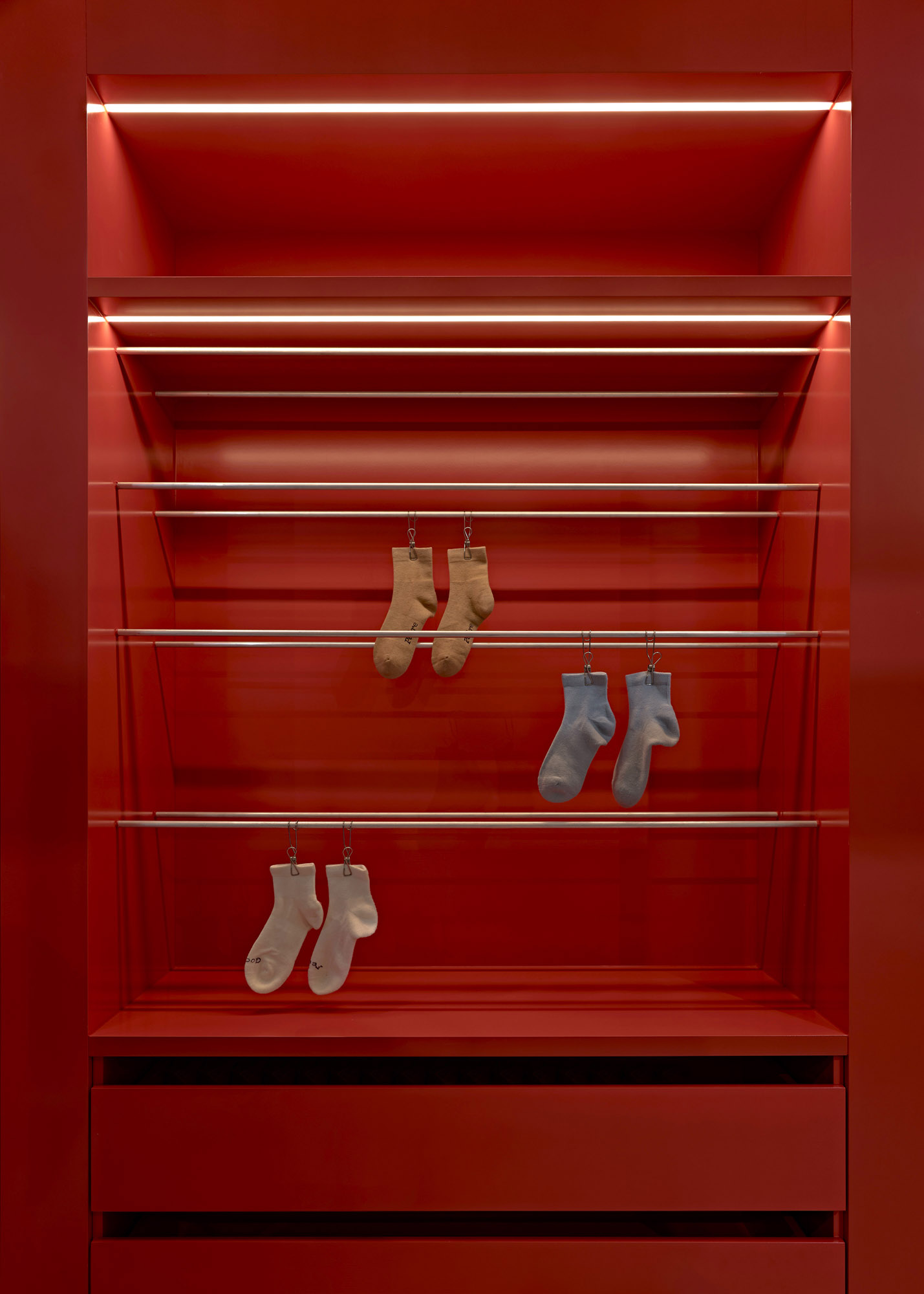 Detail of backlit red lacquer shelving bay with stainless hanging rails and socks