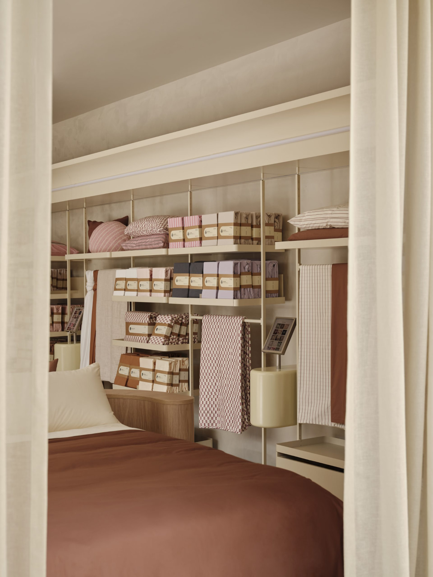 Curtained display bay with cream shelving system, bedding stock and timber bed base
